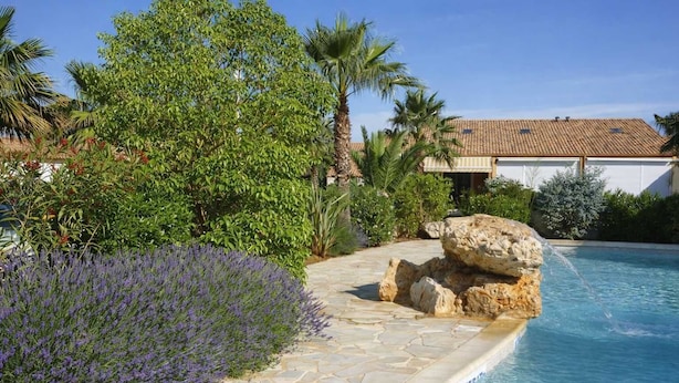 A pool with a stone pathway, surrounded by lush greenery and a large rock feature. - Clos Fontaine House with garden, pool (Valras-Plage)