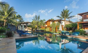 A pool with lounge chairs, a wooden deck, and a reflection of the surrounding buildings. - Apt in Condo w/ Pool in Barra Grande Vgd0001 (Maraú)