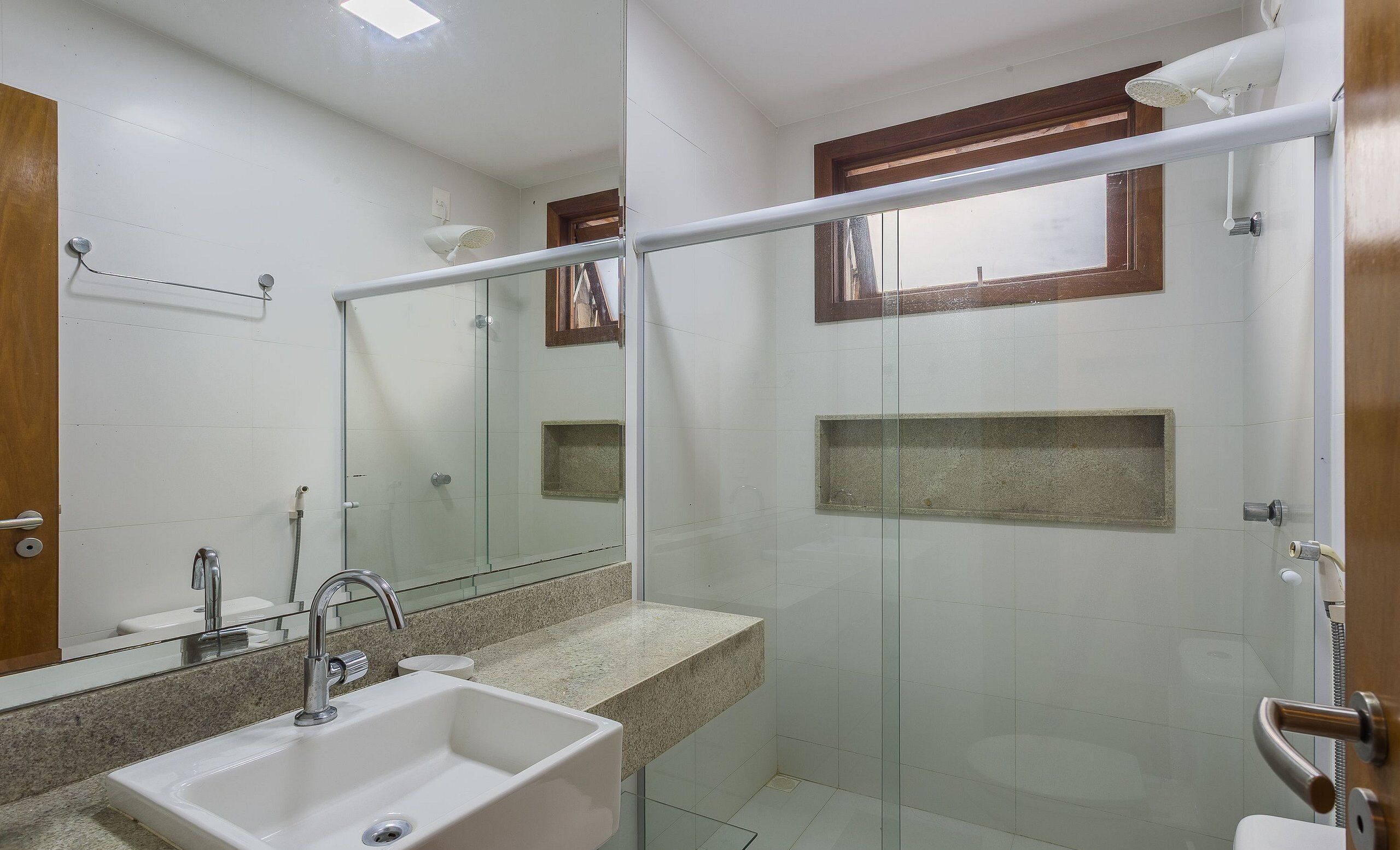 Une salle de bain avec une douche à parois de verre, un lavabo avec un miroir au-dessus et une fenêtre à cadre en bois.