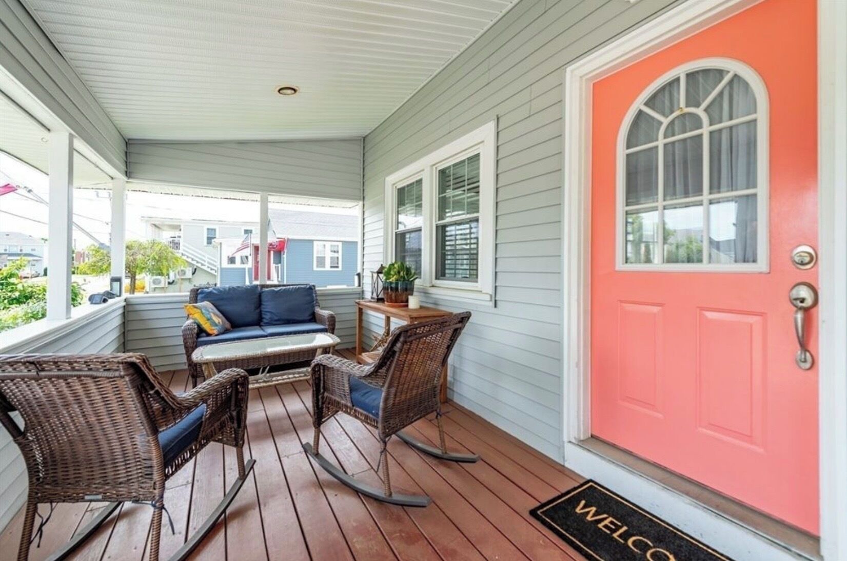 A covered porch with wicker furniture, a red door, and a welcome mat.