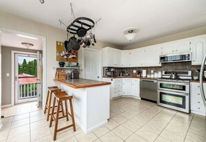 A modern kitchen with white cabinets, a central island with stools, stainless steel appliances, and a hanging pot rack. - 4 minute walk to beach in Hull’s desirable Alphabets neighborhood! (Hull)