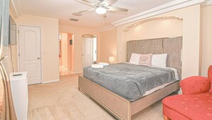 Ein Schlafzimmer mit einem Bett, einem Deckenventilator, einem Nachttisch, einem roten Sessel und einer Tür.