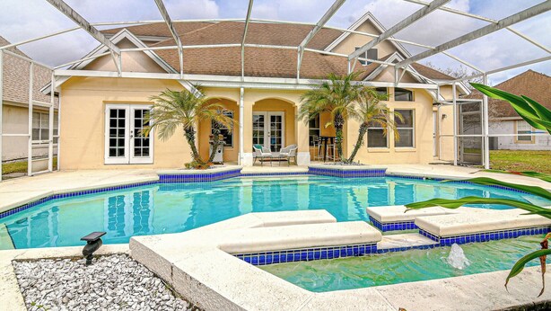 Ein Pool mit Glasdach, umgeben von einem Haus mit beige-farbener Fassade und einer gefliesten Terrasse.