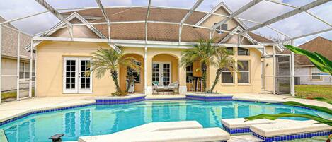 A swimming pool with a glass ceiling, surrounded by a house with a beige exterior and a tiled deck.
