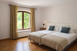A double bed with two pillows, a bedside table with a lamp, and a window with curtains.