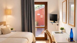 Een hotelkamer met twee bedden, een bureau, een televisie en een raam met uitzicht op een rood gebouw.