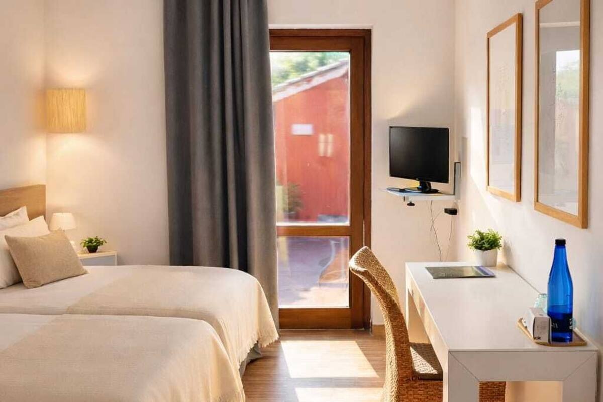 Een hotelkamer met twee bedden, een bureau, een televisie en een raam met uitzicht op een rood gebouw.