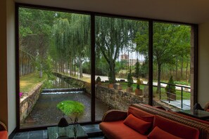 Una stanza con un'ampia finestra su un giardino con fontana e alberi.