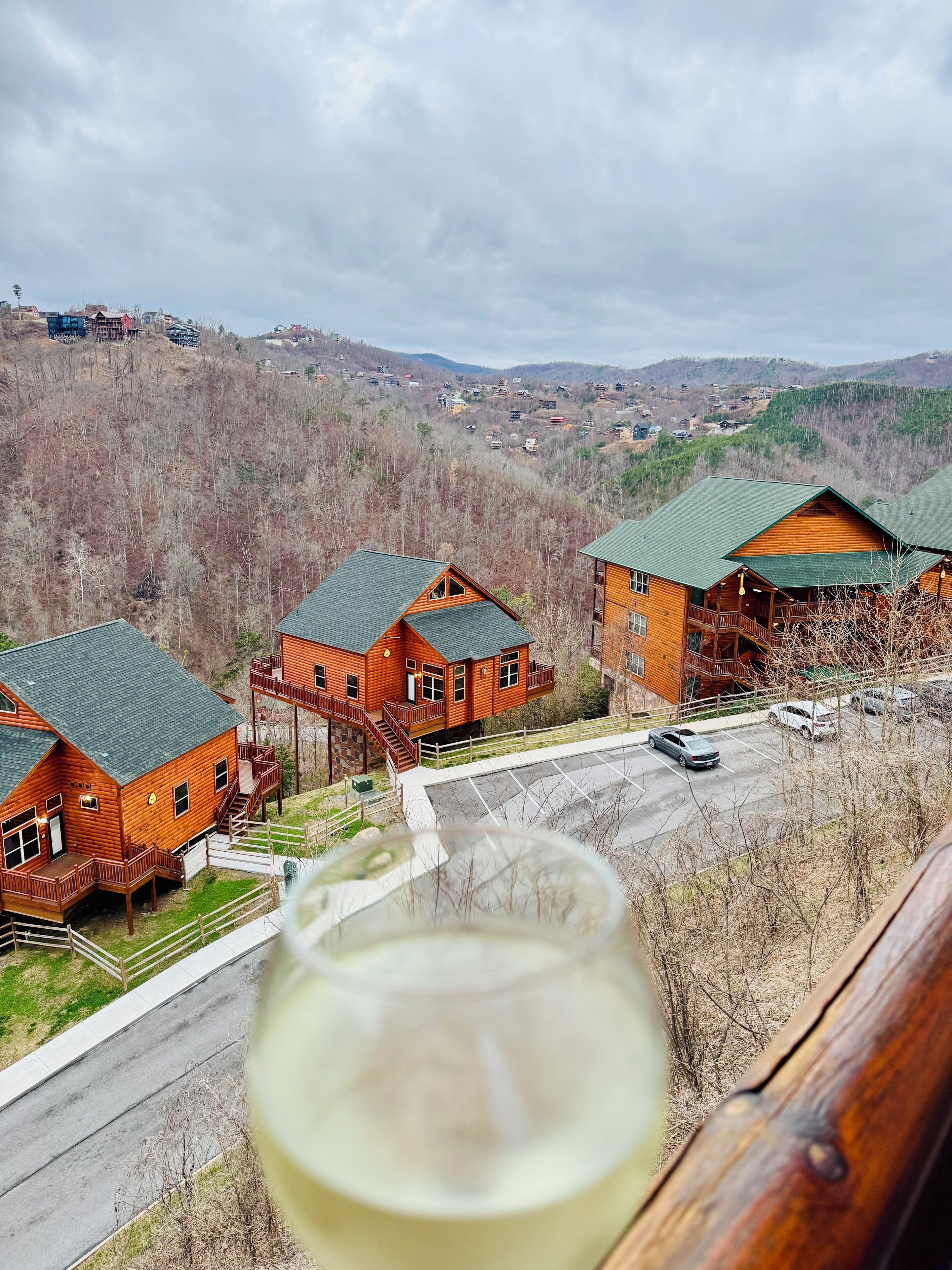 Eine Holzhütte mit Balkon, Parkplatz und Blick auf ein bewaldetes Tal.