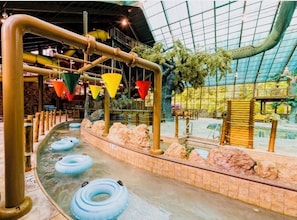 Un toboggan aquatique intérieur doté de plusieurs pistes, d’un toit en verre et d’un décor rocheux.