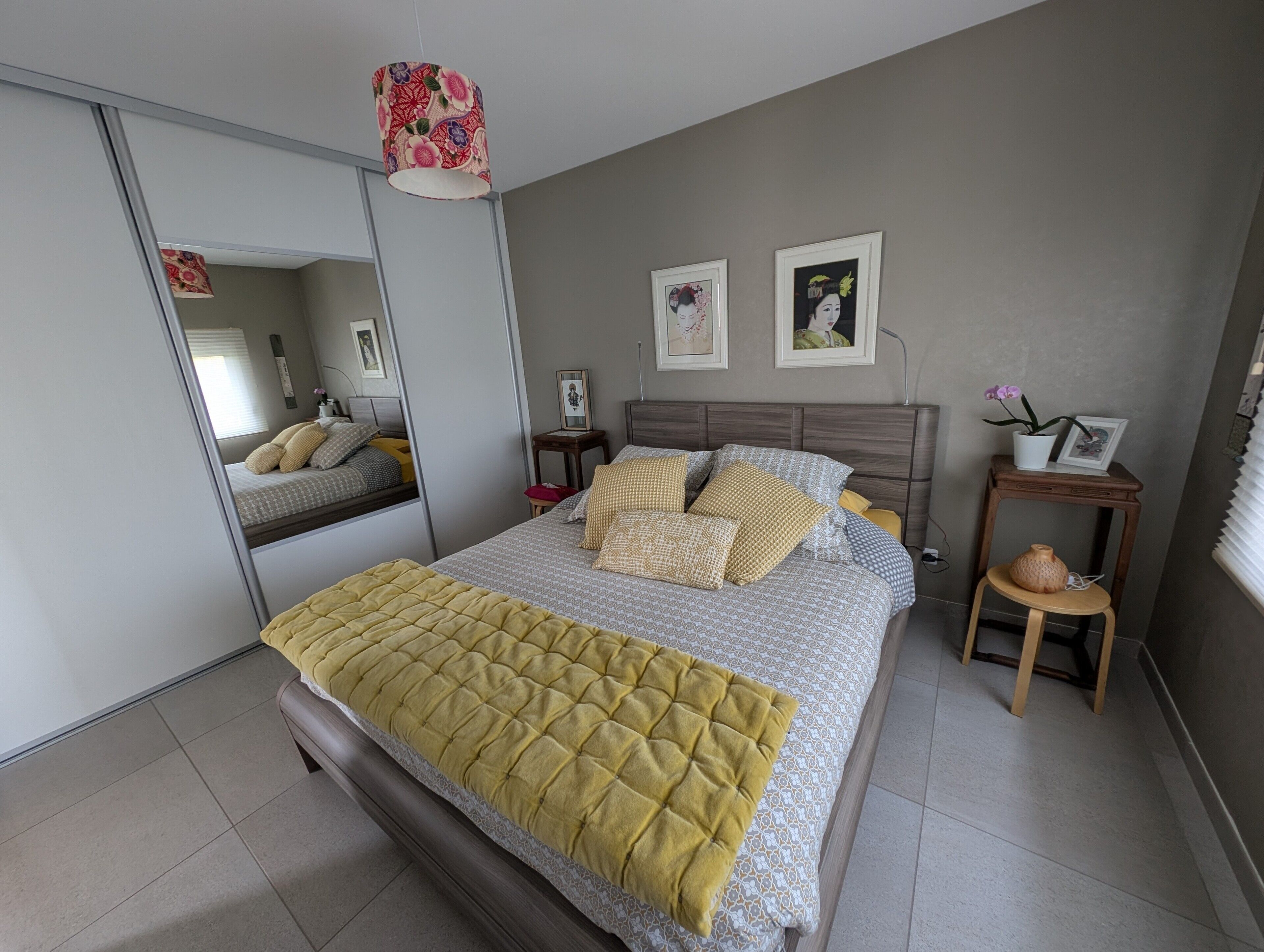 A bedroom with a bed, a bedside table, a mirror, and a small stool.