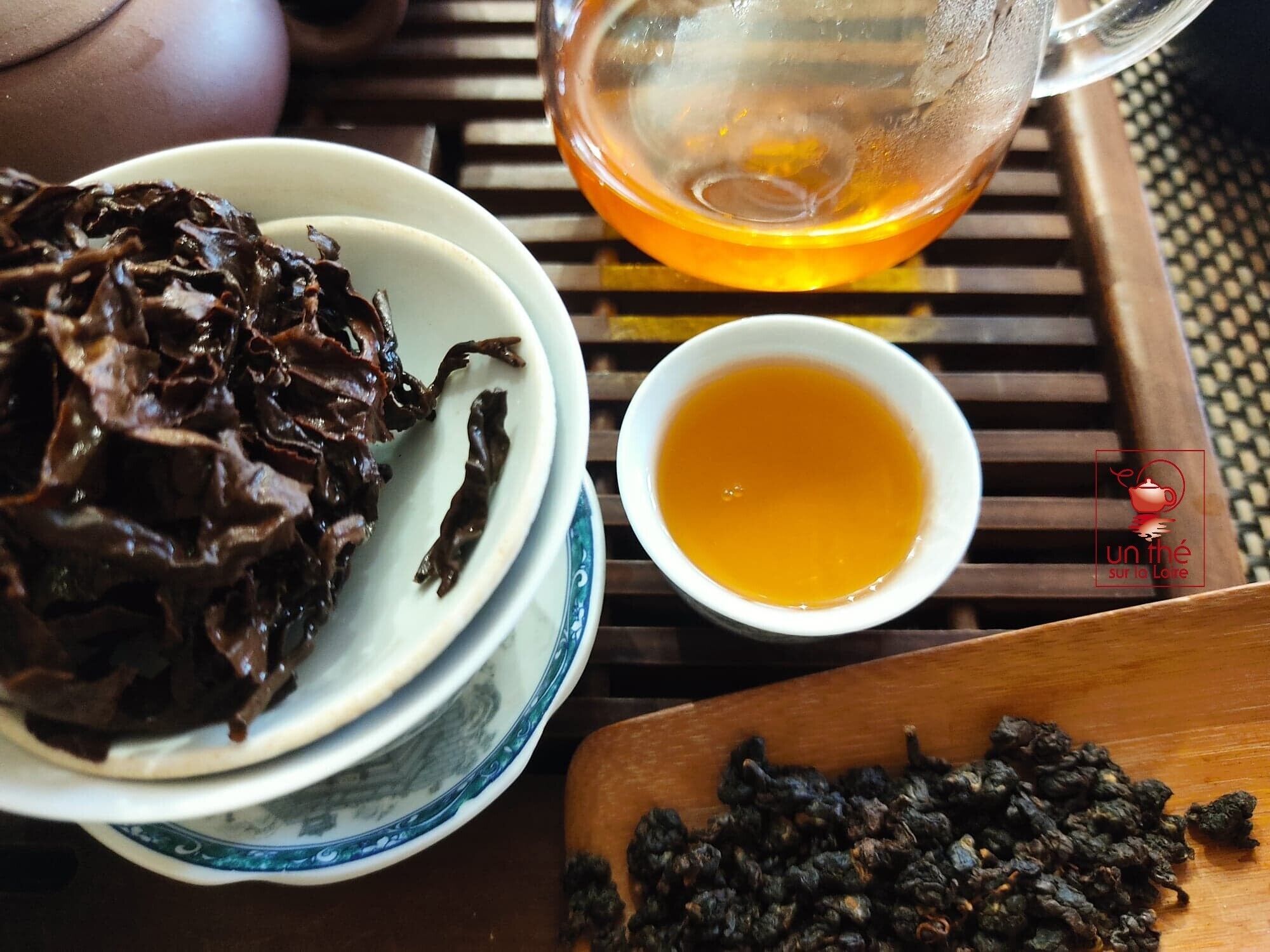 A table with a bowl of dried tea leaves, a cup of tea, and a wooden board with more tea leaves.
