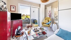 Een moderne woonkamer met een glazen salontafel, een bank, een rode kast, een televisie en een schuifpui naar een buitenruimte.