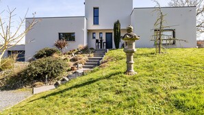 Een modern herenhuis met twee verdiepingen en een trap naar de ingang, omringd door een verzorgde tuin.