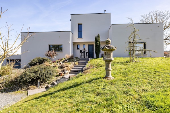 A modern two-story house with a staircase leading to the entrance, surrounded by a well-maintained garden.