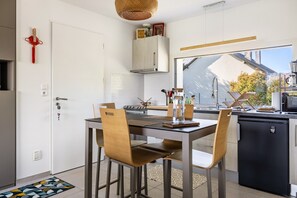 A modern kitchen with a dining table, chairs, and a refrigerator.