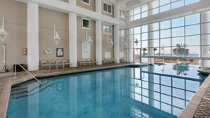 En indendørs swimmingpool med glasvægge, flere niveauer og havudsigt.