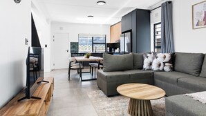 A modern living room with a grey sofa, a wooden coffee table, and a dining area with a table and chairs.