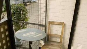 Uma varanda com uma mesa redonda e uma cadeira de madeira, um muro de tijolos brancos e um corrimão de metal.