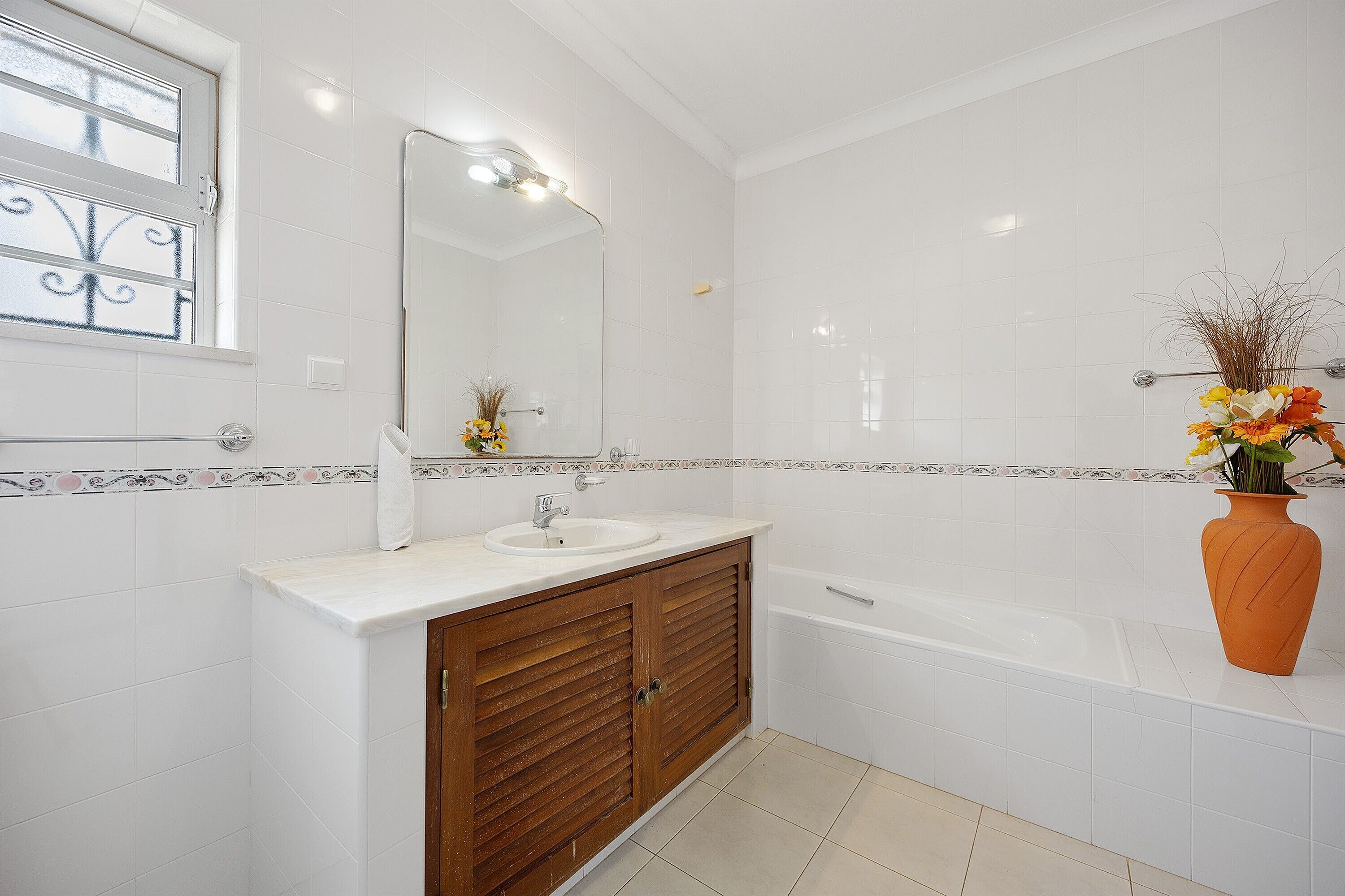 Un bany amb un lavabo blanc, mobles de fusta, un mirall i una banyera.