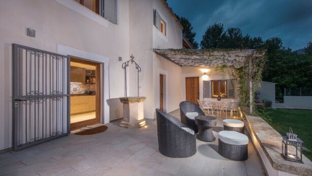 Eine Terrasse im Freien mit Korbmöbeln, einem Steintisch und einer Pergola.