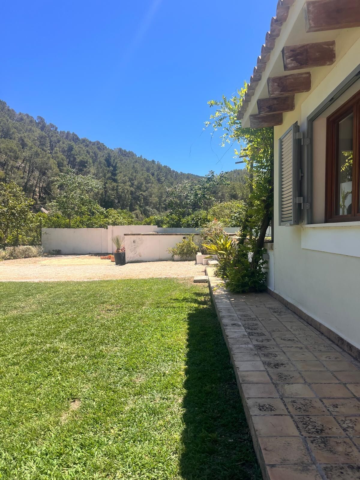 A residential property with a well-maintained lawn, a paved patio, and a view of a forested hill.