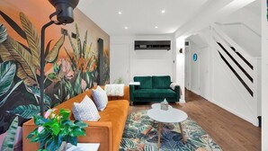 A modern living room with a sofa, a coffee table, a green couch, and a large plant. - Stylish 4 Bedroom 2 Bath House with Canal Views (London)