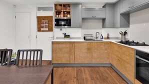 A modern kitchen with grey cabinets, a wooden island, and a dining area with a dark wooden table and chairs. - Stylish 4 Bedroom 2 Bath House with Canal Views (London)