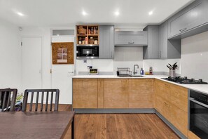 Une cuisine moderne avec des meubles gris, un îlot central en bois et un coin repas comprenant une table et des chaises en bois foncé.