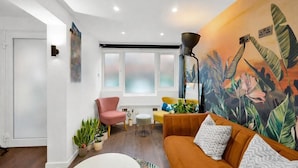 A living room with a sofa, a pink chair, a small table, and a large window. - Stylish 4 Bedroom 2 Bath House with Canal Views (London)