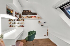 Ein modernes Interieur mit weißen Wänden, Holzdielen und einem grünen Sessel. Regale sind mit verschiedenen Gegenständen gefüllt.
