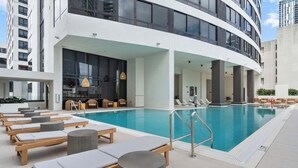 A rooftop pool area with lounge chairs, a bar, and a modern building in the background. - Downtown 2-Bed | Free Metromover | Resort Pool (Miami)