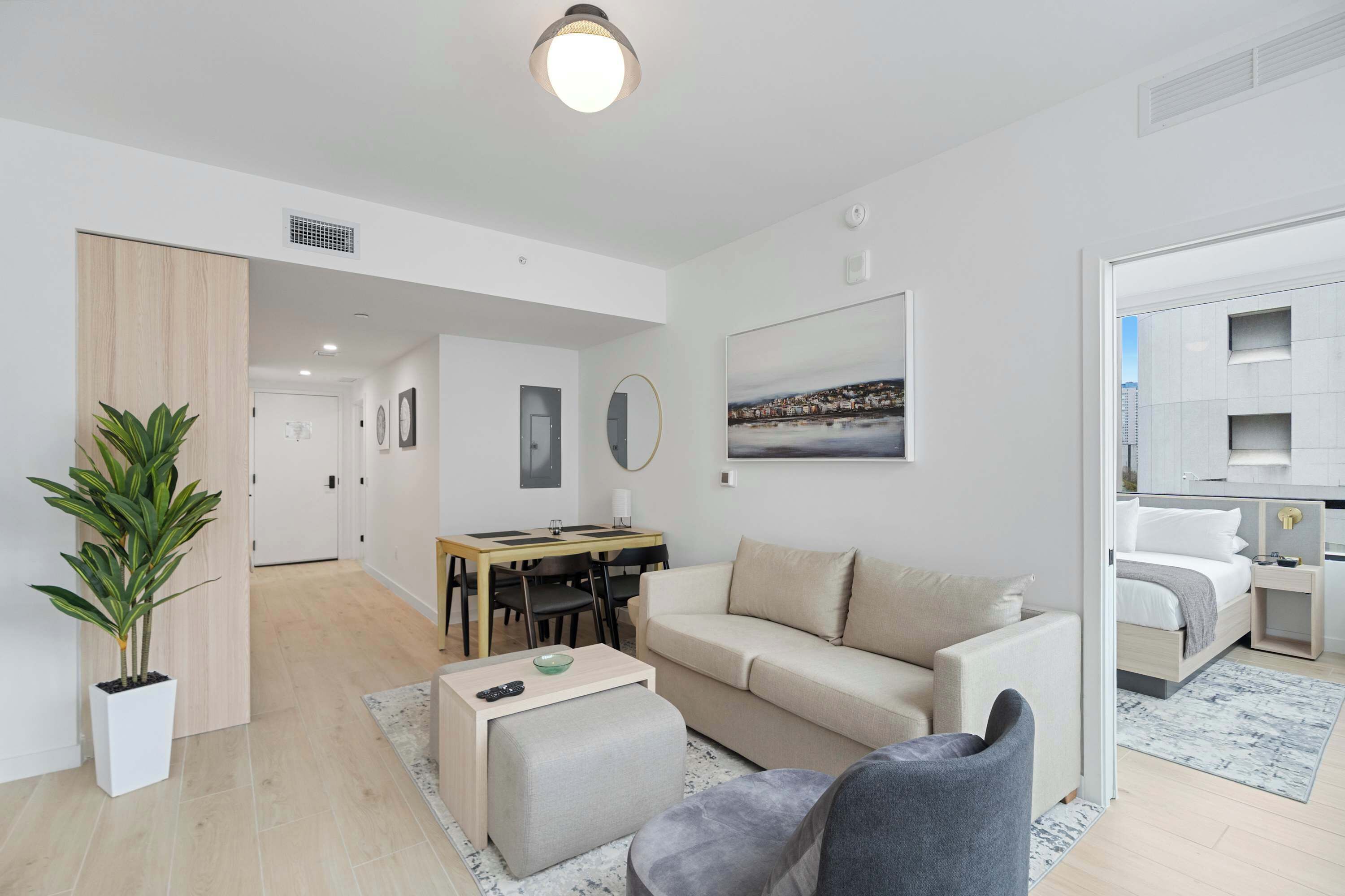 A modern living room with a sofa, ottoman, and a dining area with a table and chairs.