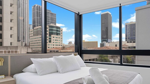 A hotel room with a large bed, white bedding, a grey throw, and a view of tall buildings. - Downtown 2-Bed | Free Metromover | Resort Pool (Miami)