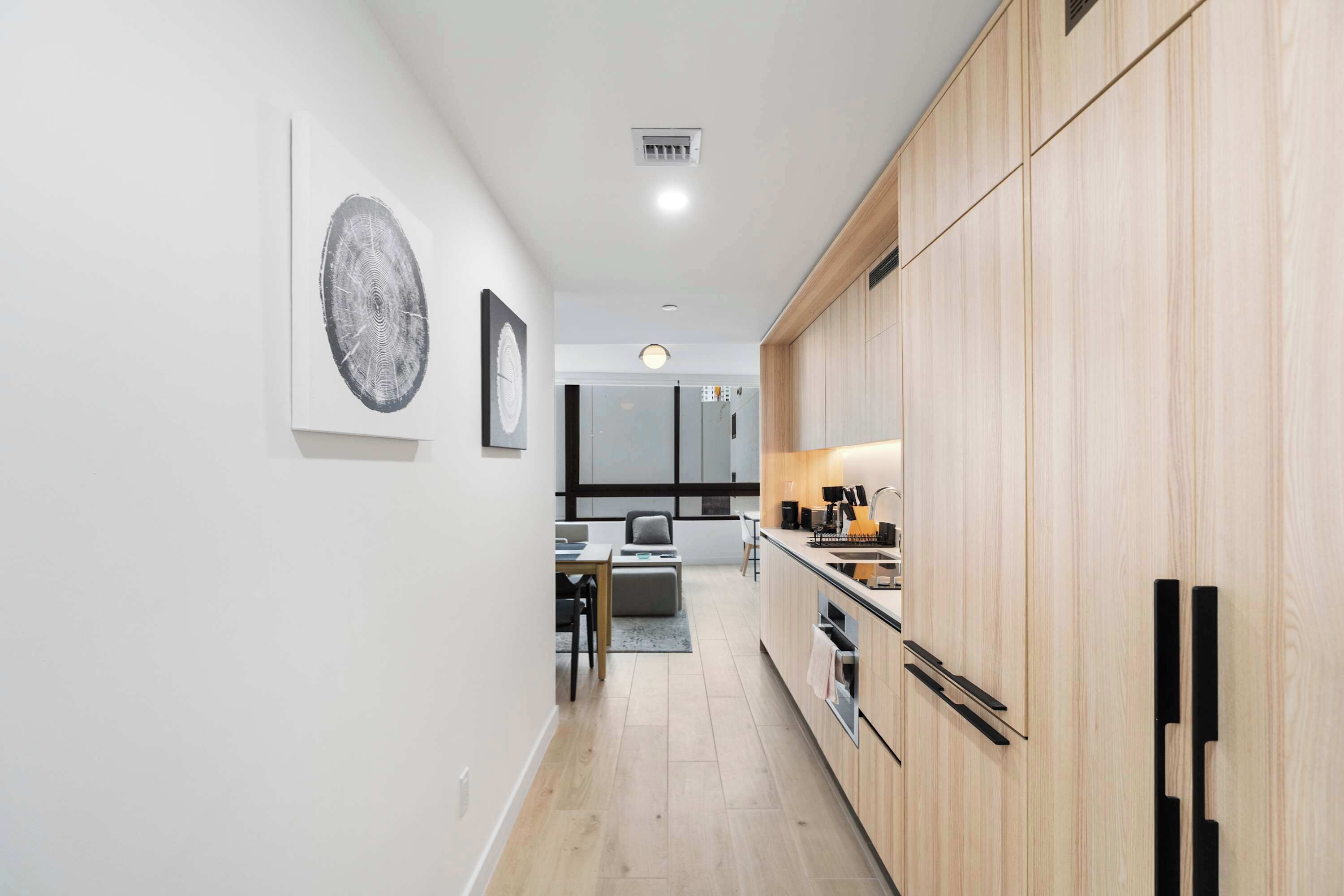 Una cocina moderna con armarios de madera, un comedor con sofá gris y obras de arte en las paredes.
