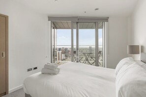 Une chambre d’hôtel avec un grand lit, un balcon donnant sur la ville et une table à l’extérieur.