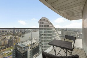 Un immeuble de grande hauteur à la façade incurvée, offrant une vue sur une rivière et doté d’un balcon avec une table et des chaises.