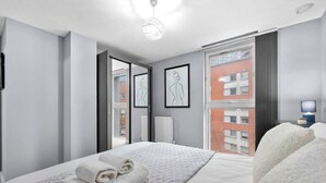 A modern hotel room with a bed, a large window, and artwork on the wall. - 2-bedroom apartment near Canary Wharf (London)
