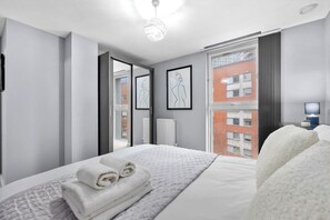 A modern hotel room with a bed, a large window, and artwork on the wall. - 2-bedroom apartment near Canary Wharf (London)