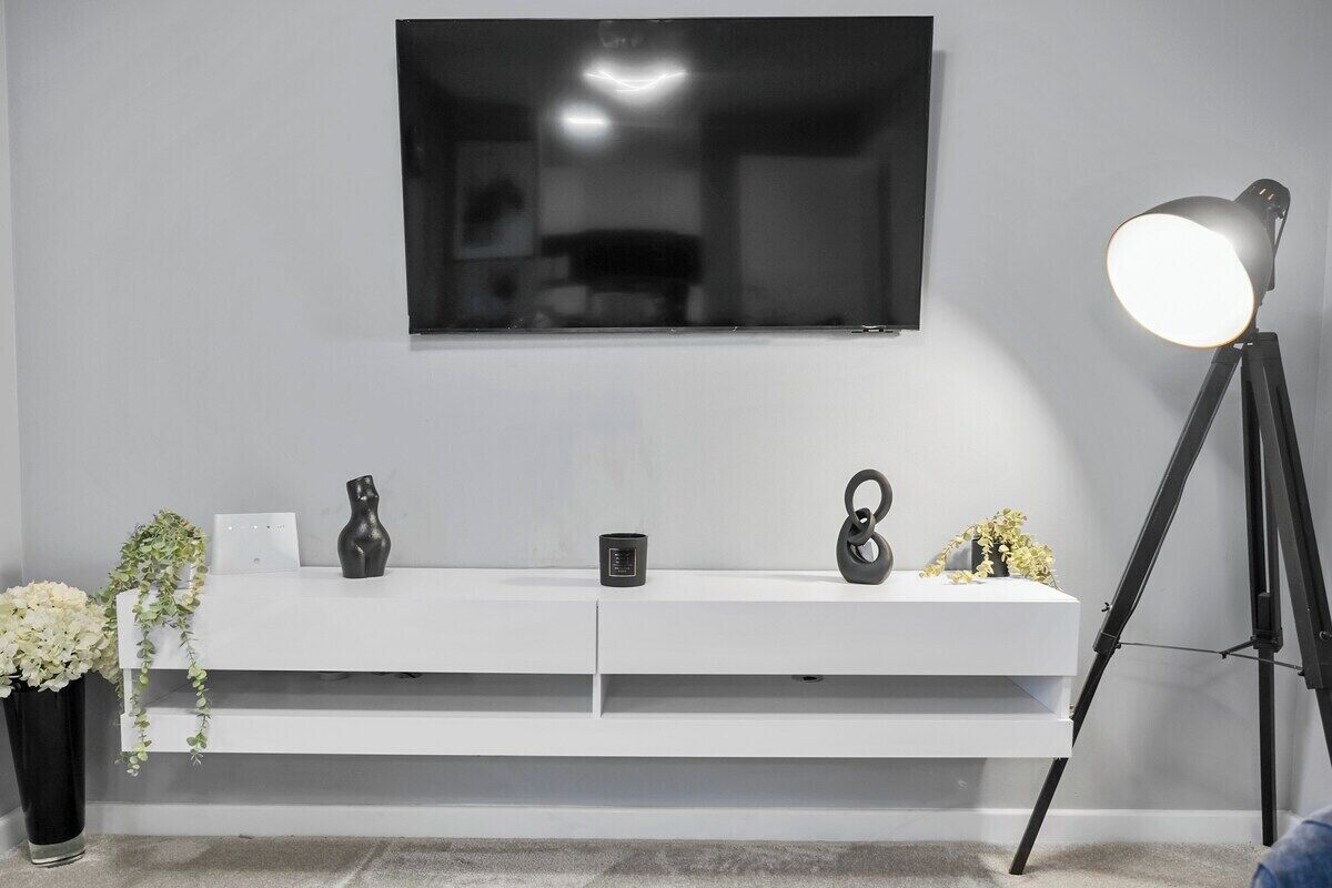 A modern living room with a white console table, a mounted flat-screen TV, a floor lamp, and a potted plant.