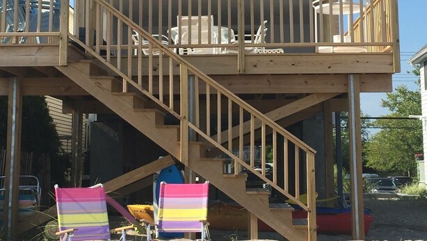 Ein zweistöckiges Haus mit einer Holzterrasse, einer Treppe und Sitzgelegenheiten im Freien.