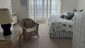 Ein Schlafzimmer mit einem Bett, einem Korbstuhl, einem Glastisch und einem Deckenventilator.
