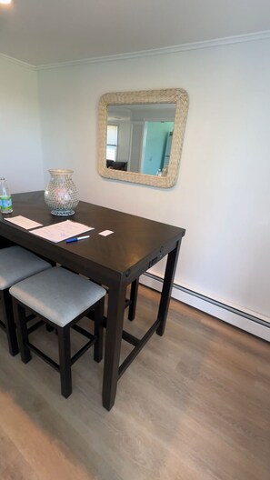 Une table à manger avec un plateau en bois foncé, un miroir à motifs tissés au-dessus, et un vase orné de motifs en mosaïque sur la table.