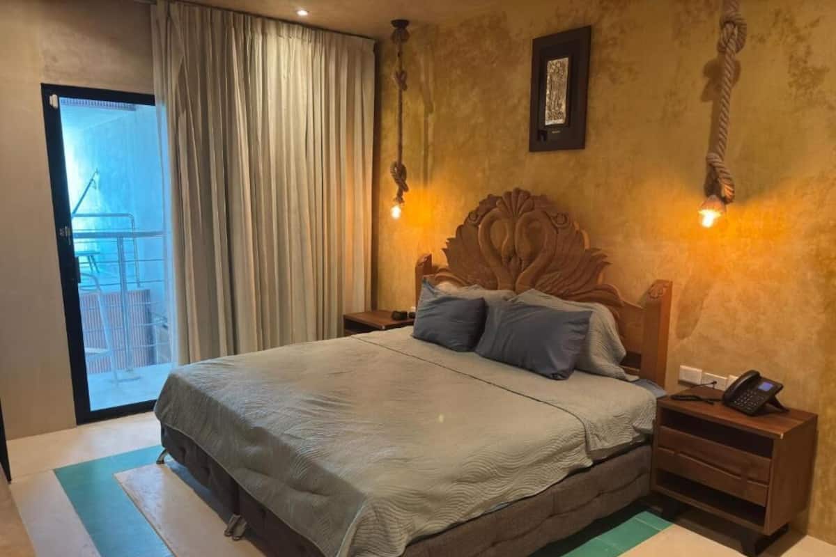 A bedroom with a large bed, a wooden headboard, two bedside tables with lamps, and a view of a balcony through a glass door.