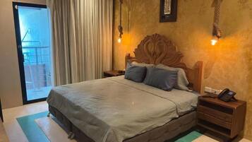 Un dormitorio con una cama grande, un cabecero de madera, dos mesitas de noche con lámparas y vistas a un balcón a través de una puerta de cristal.
