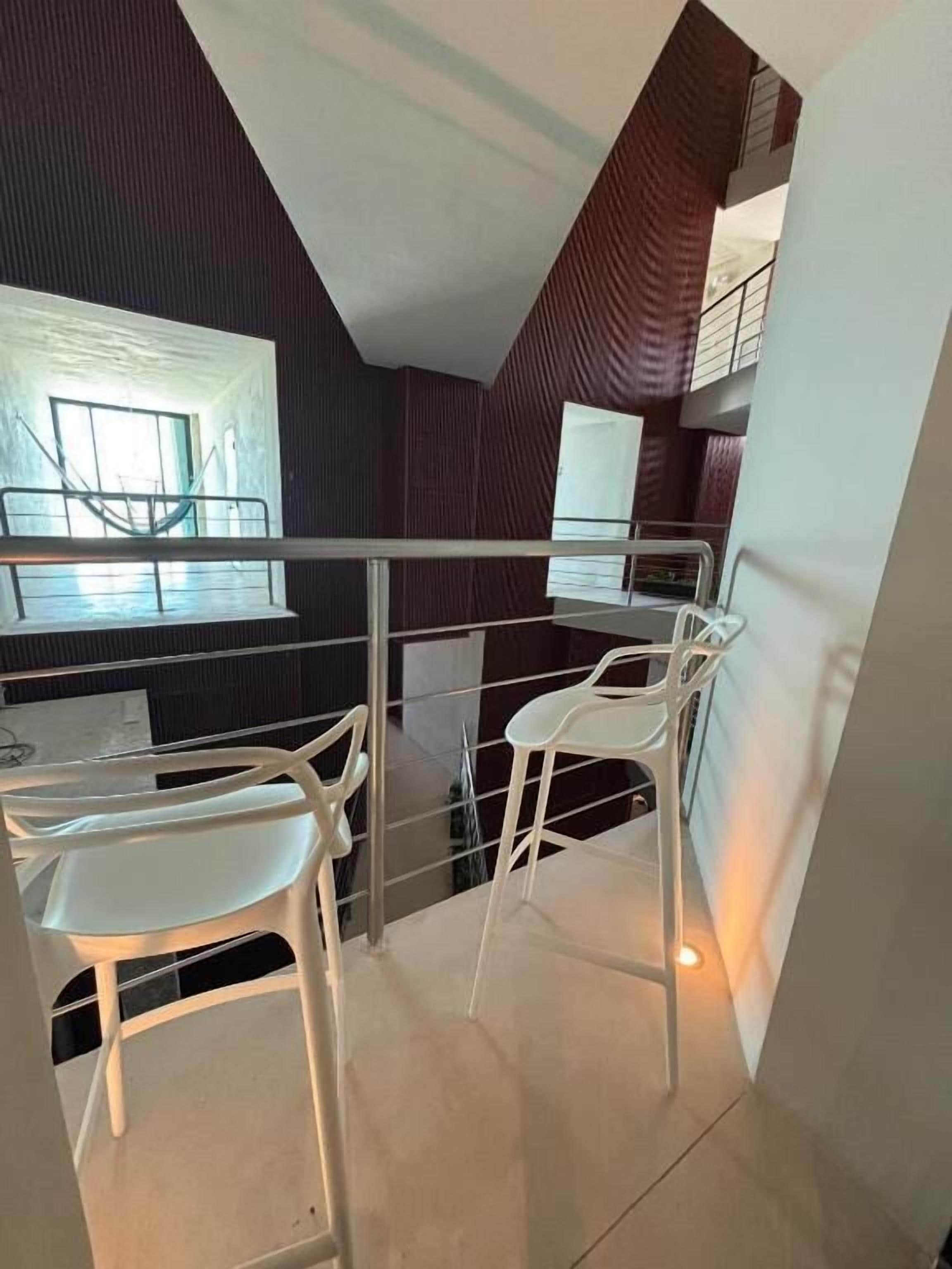 Un interior moderno con comedor, sillas blancas y barandilla de vidrio.