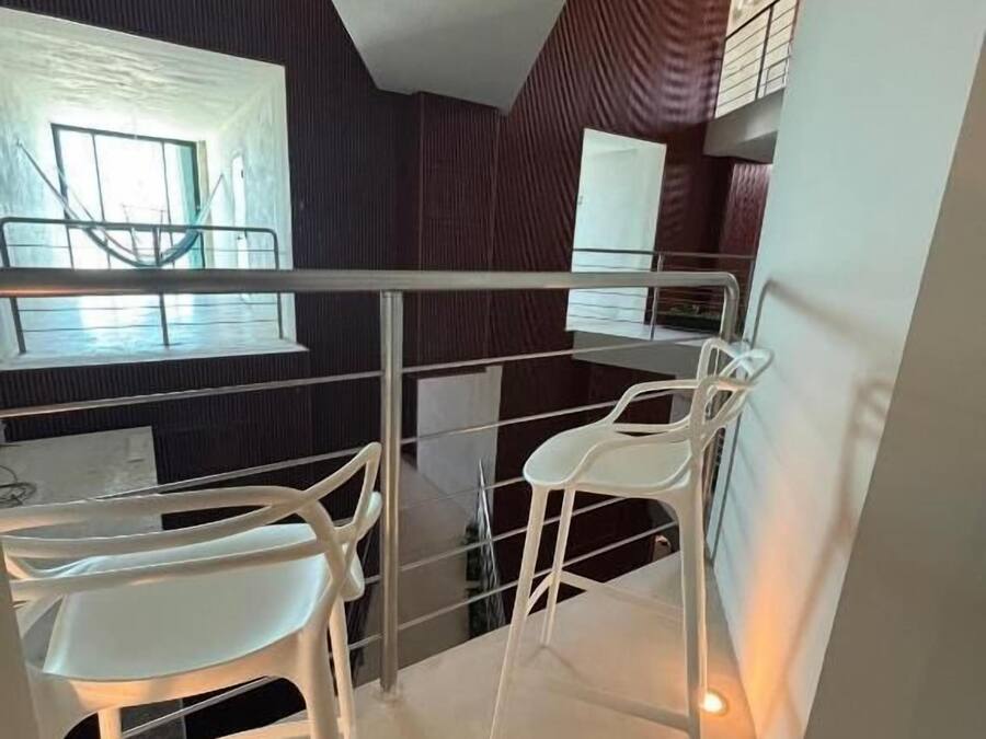 Un interior moderno con comedor, sillas blancas y barandilla de vidrio.