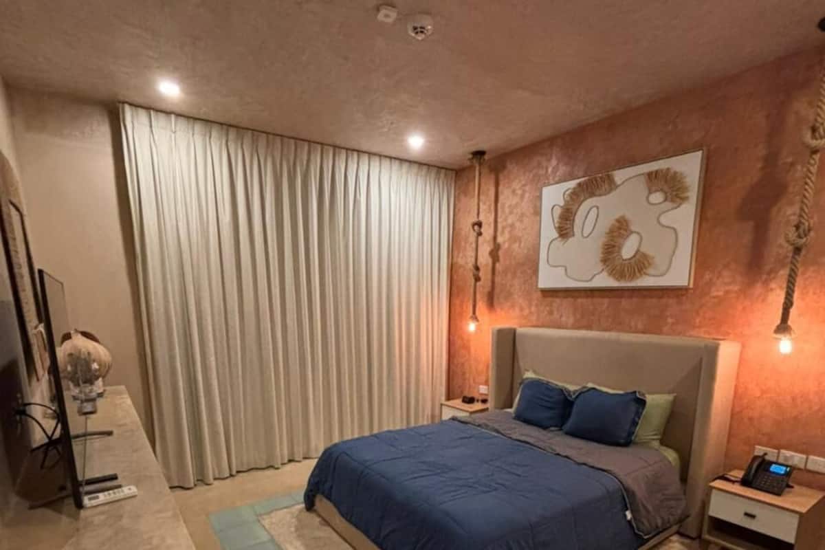 A bedroom with a bed, a desk, a chair, a TV, and a curtain.