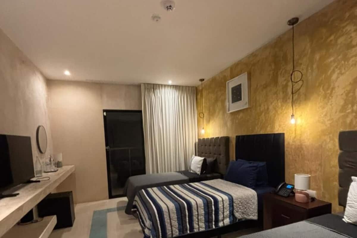 A hotel room with a bed, bedside tables, a desk with a chair, a TV, and a window with curtains.