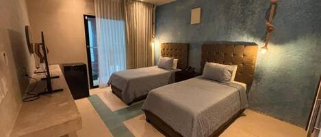 A hotel room with two beds, a desk, a trash bin, and a window with curtains.